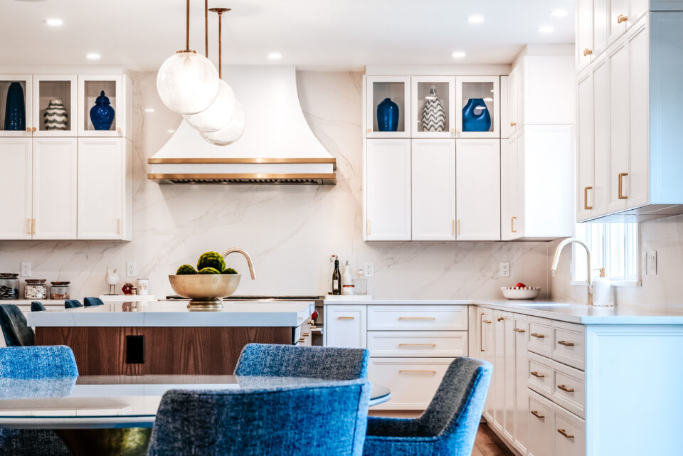 Spacious open-concept kitchen with white cabinetry, wood-accented island, designer lighting, and upholstered dining chairs in a modern interior.