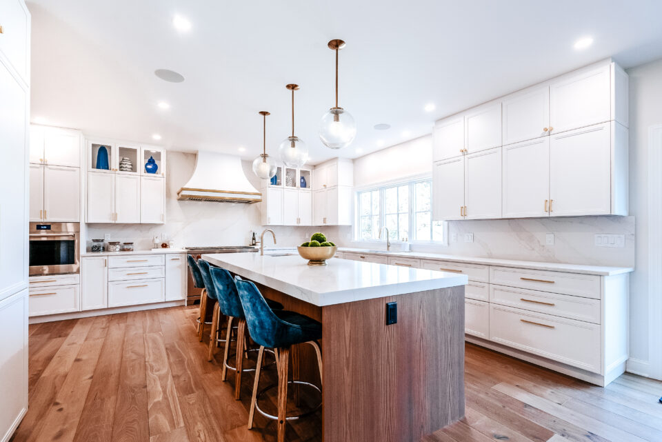Modern kitchen in Wyckoff NJ featuring a waterfall island, sleek white cabinetry, and natural wood flooring with designer lighting and seating.