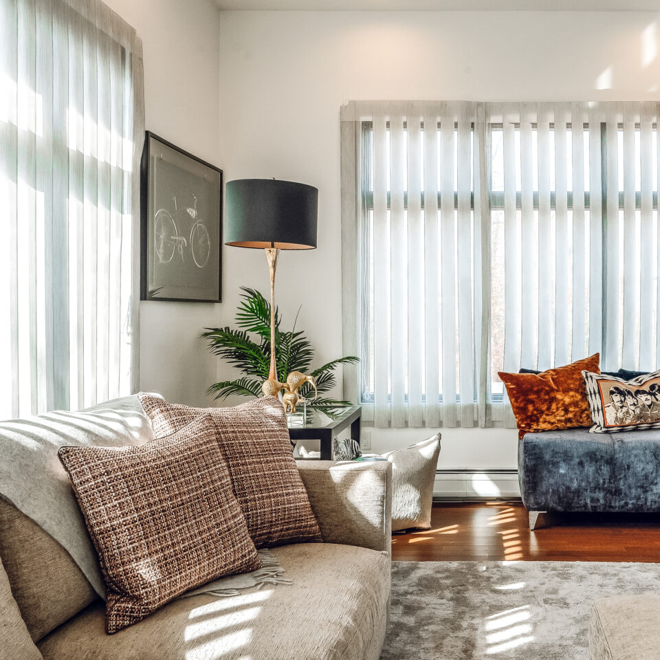 Sunlit sitting room corner with neutral-tone sofa, textured accent pillows, modern black floor lamp, and soft window treatments.